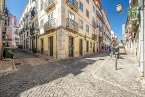 A cobblestone street lined with historic buildings, a parked motorcycle, and a group of people walking. - GuestReady-Charming Lisbon Retreat (Lisbon)