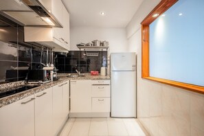 A compact kitchen with white cabinets, a built-in oven, a stainless steel sink, and a white refrigerator. - GuestReady-Charming Lisbon Retreat (Lisbon)