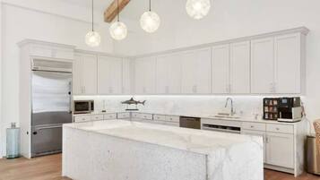 Une cuisine moderne avec des meubles blancs, un grand îlot central, des appareils en acier inoxydable et des luminaires suspendus.