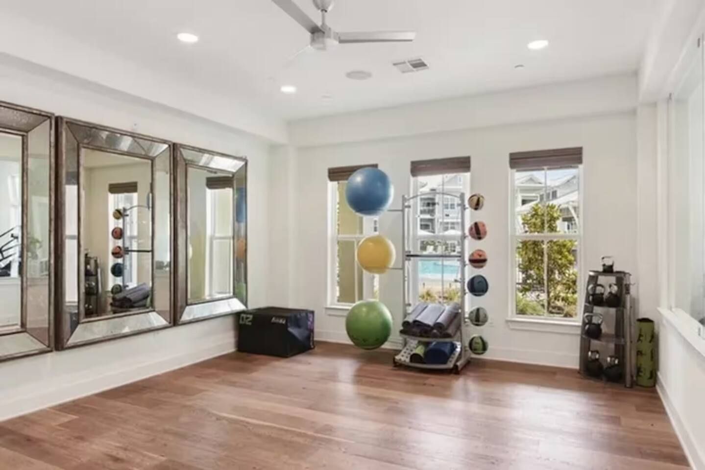 Una habitación amplia con piso de madera, espejos grandes, equipo de ejercicio y ventanas con vistas.