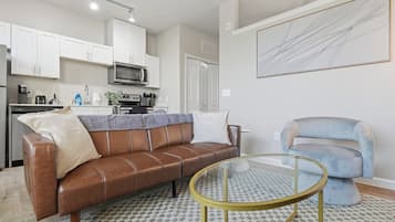 A modern living room with a brown leather sofa, a round glass coffee table, and a light blue armchair.