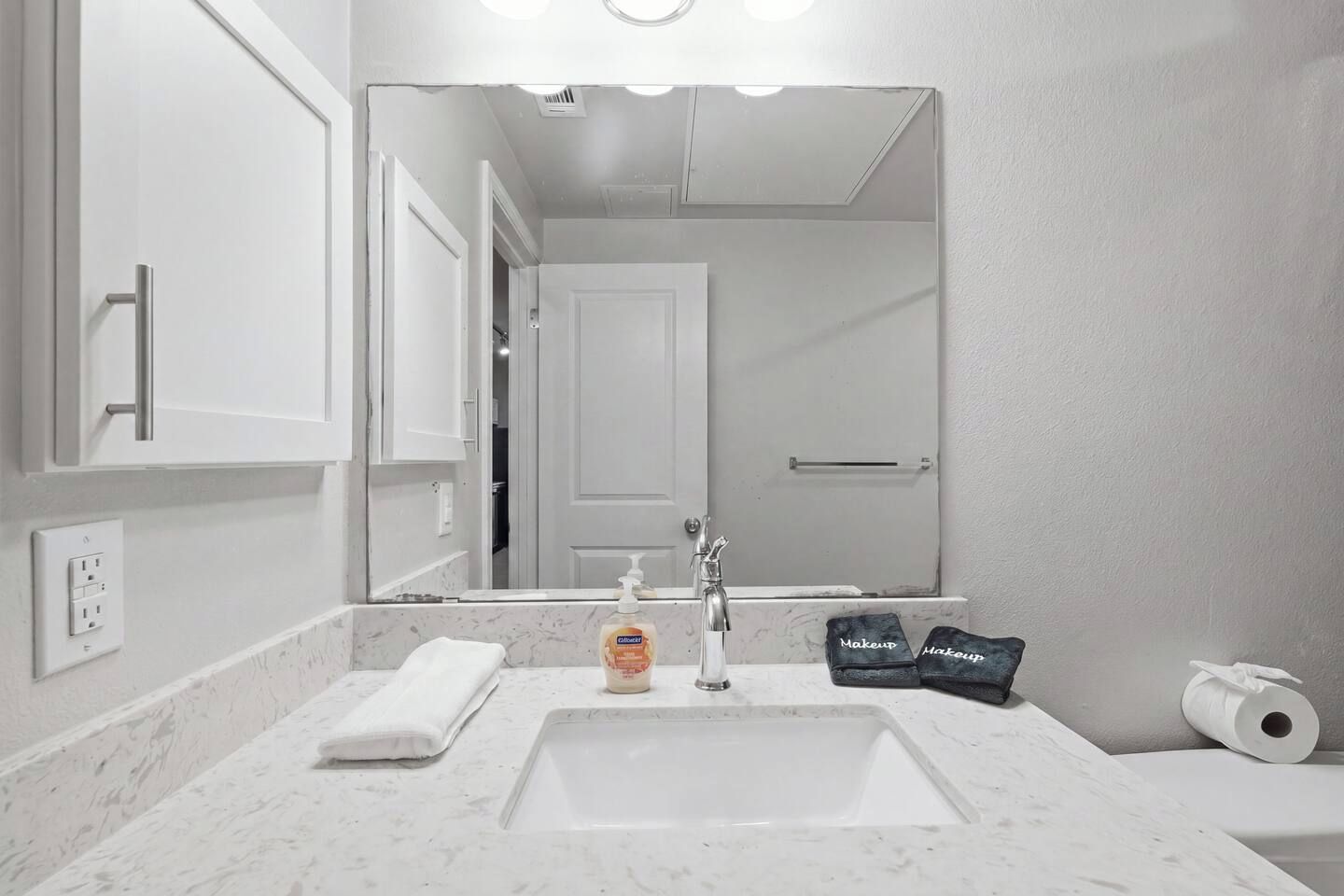 A bathroom with a white sink, a mirror, a towel, a bottle of soap, and a toilet paper roll.