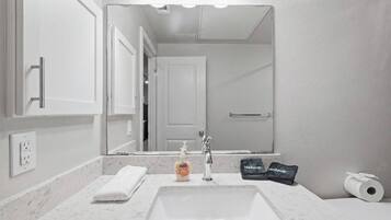 A bathroom with a white sink, a mirror, a towel, a bottle of soap, and a toilet paper roll.