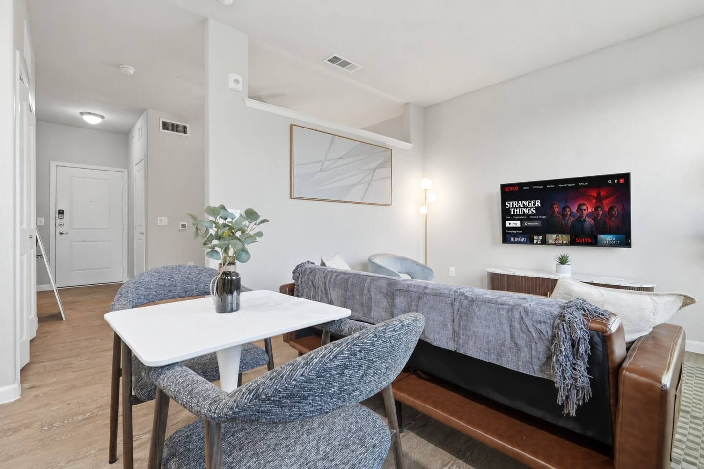 A modern living room with a dining table, two chairs, a sofa, and a TV displaying a movie.