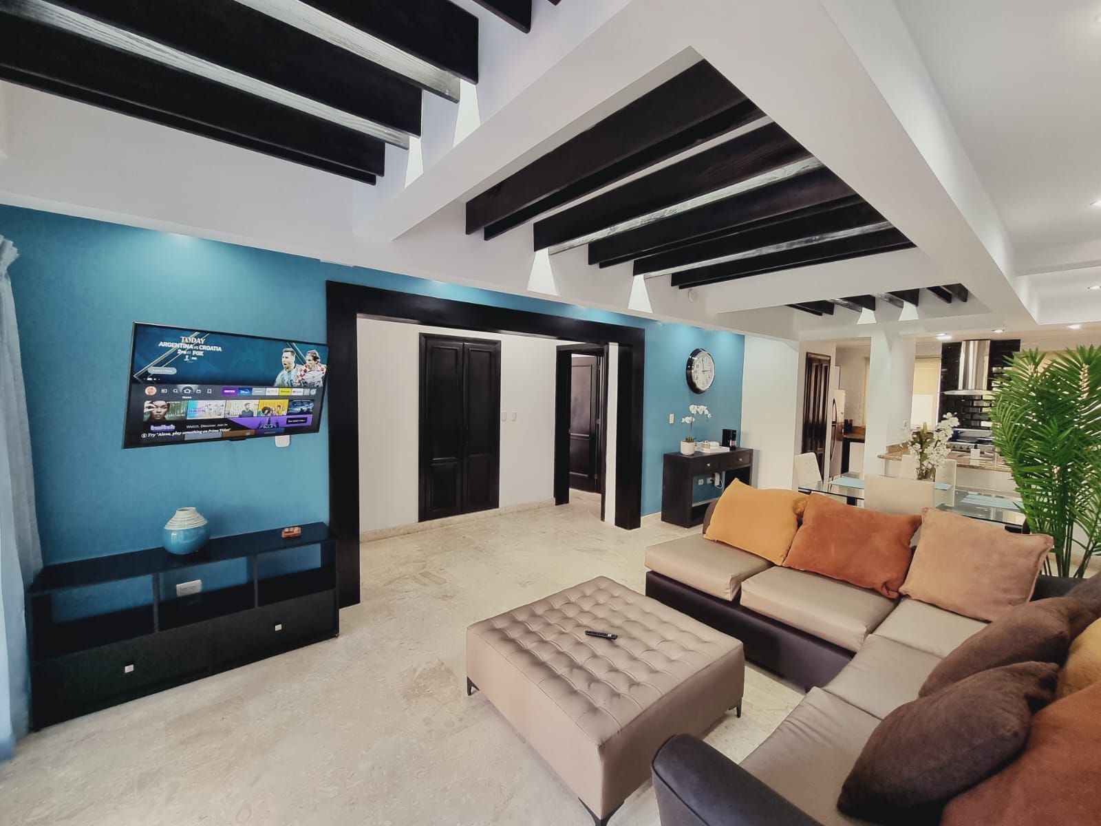 A modern living room with a flat-screen TV, a sofa set, a coffee table, and a large window.