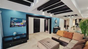 A modern living room with a flat-screen TV, a sofa set, a coffee table, and a large window.