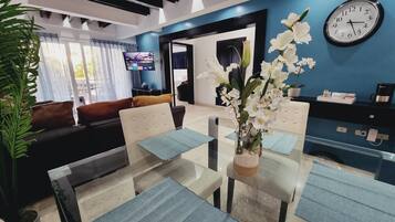 A modern living room with a glass dining table, a sofa, and a TV in the background.