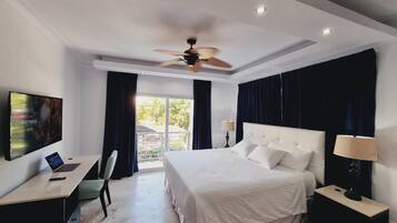 A hotel room with a bed, a desk with a laptop, a TV, and a ceiling fan.