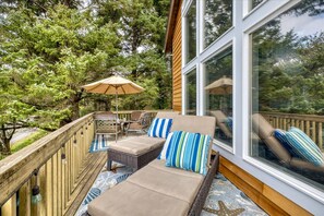 Eine Terrasse mit Gartenmöbeln, darunter Liegestühle und ein Tisch, umgeben von einem Holgitter und großen Fenstern.