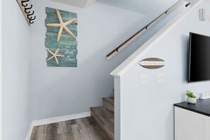 A staircase with a wooden handrail, a wall-mounted sign reading 'Welcome to our Beach House,' and a flat-screen TV on the wall. - Sunshine & Shenanigans- Steps to Main Pool & More! (Panama City Beach)