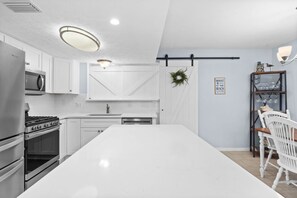 A modern kitchen with white cabinetry, a stainless steel refrigerator, a built-in oven, and a large island. - Sunshine & Shenanigans- Steps to Main Pool & More! (Panama City Beach)