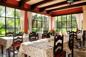 Comedor con mesas dispuestas para cuatro, ventanas amplias con cortinas y vista a zonas verdes.