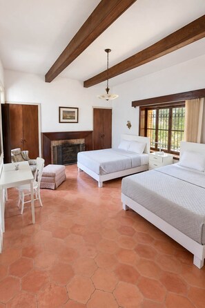 A bedroom with two beds, a desk, a chair, a fireplace, and large windows.