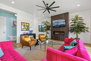 A modern living room with a fireplace, two leather armchairs, a bright pink sofa, and a ceiling fan. - Flagstaff Barbie House - 2 King Suites & Fire Pit, Hot Tub (Flagstaff)