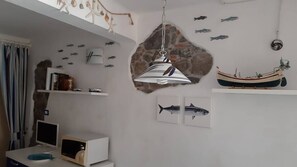 Ein Zimmer mit weißer Wand, einer Hängelampe, einer Wandsticker-Darstellung von Fischen, einem kleinen Bootsmodell und einem Computer auf einem Schreibtisch.