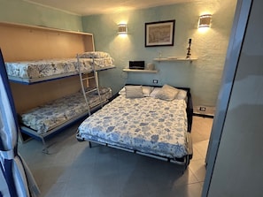 Ein Schlafsaalzimmer mit Etagenbetten, einem Schreibtisch, einem Stuhl, einem Regal mit einem Bild und einer Wandleuchte.