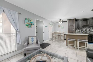 Ein modernes Wohnzimmer mit einem grauen Sofa, einem Glastisch und einem Essbereich mit Tisch und Stühlen.