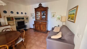 Una sala de estar con sofá, mesa de comedor, sillas, televisor, aparador y adornos en la pared.