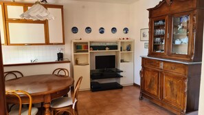 A dining area with a wooden table and chairs, a television on a stand, and a cabinet with glass doors. - La Terrazza sul Mare Sea View - near best beaches (Monterosso al Mare)
