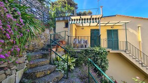 Una escalera de piedra que lleva a un edificio amarillo con contraventanas verdes y un balcón.