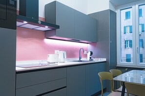 Eine moderne Küche mit grauen Schränken, einer pinkfarbenen Spritzschutzleiste und einem Fenster mit Blick auf ein Gebäude mit blauen Fensterläden.