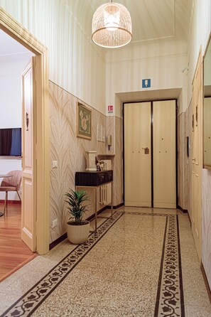 A hallway with a patterned carpet, a potted plant, a framed picture on the wall, and a door with a sign above it. - Lele Rooms Vaticano (Roma)