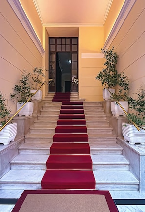 Eine prächtige Treppe mit roten Teppichstufen führt zu einer dunklen Tür.