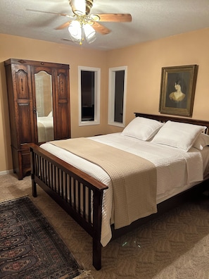 A bedroom with a wooden bed, a ceiling fan, a painting, and a mirror.