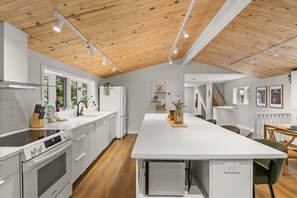 A modern kitchen with white cabinetry, a central island, and a wooden ceiling. - HAMAC | Spa & Lake Access in Dunham (Dunham)