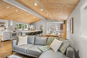 A modern kitchen with a central island, a dining area with a wooden table, and a living room with a grey sofa.