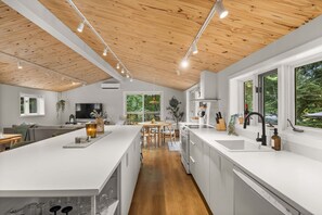 A modern kitchen with white cabinetry, a wooden ceiling, and large windows.