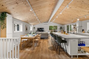 A modern kitchen with a wooden ceiling, a dining area with a table and chairs, and a bar area with stools. - HAMAC | Spa & Lake Access in Dunham (Dunham)