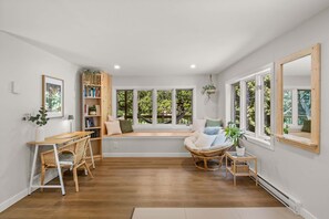 A room with a large window, a bookshelf, a wicker chair, and a cushioned seating area. - HAMAC | Spa & Lake Access in Dunham (Dunham)