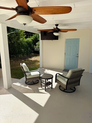 Eine überdachte Terrasse mit zwei Korbstühlen, einem kleinen runden Tisch und Deckenventilatoren.