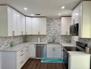 A modern kitchen with white cabinets, a stainless steel dishwasher, a built-in oven, and a microwave. - Newly renovated custom 3-bedroom/ 2 bath house in coastal area! (West Palm Beach)