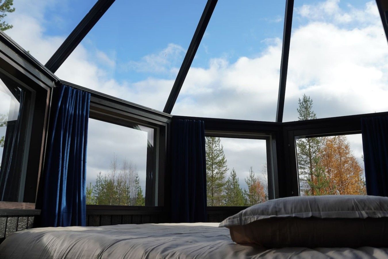 A room with a bed, a window, and a view of trees and sky.