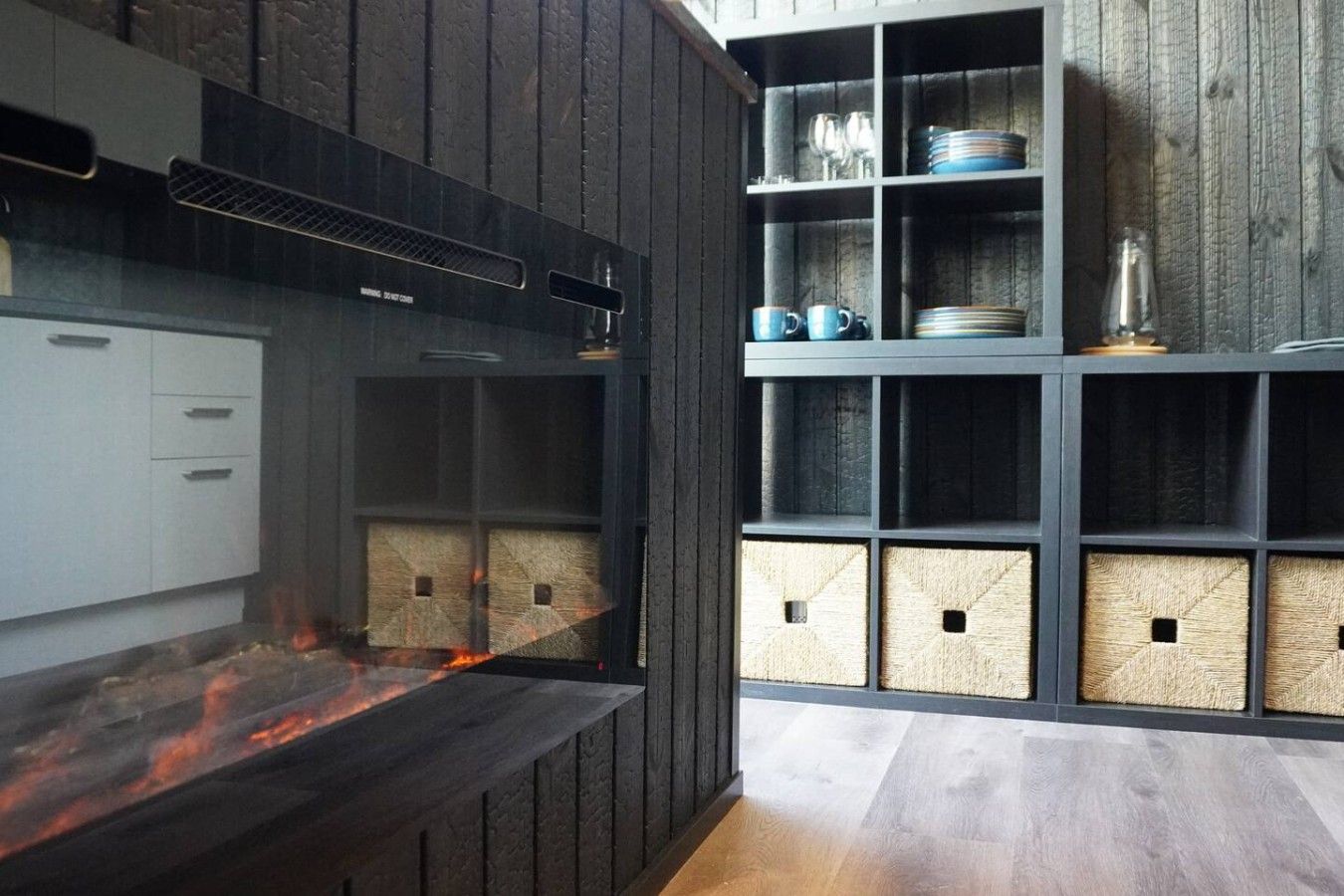 A modern kitchen with a built-in stove, wooden cabinets, and a shelving unit with dishes and glasses.