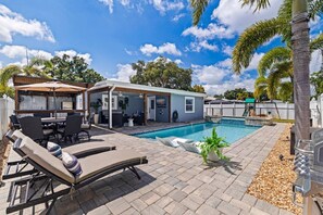 Ein Garten mit Swimmingpool, Liegestühlen, Grill und überdachter Terrasse.
