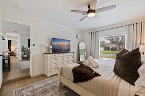 A bedroom with a bed, a dresser, a ceiling fan, and a large window. - St Pete Poolside Paradise w/ Outdoor Bar (St. Petersburg)