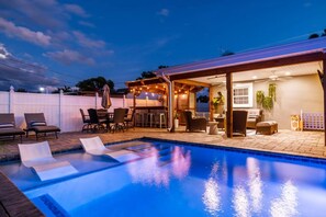 A swimming pool with lounge chairs, a covered patio area with seating, and a view of the sky. - St Pete Poolside Paradise w/ Outdoor Bar (St. Petersburg)