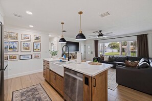A modern kitchen with a central island, wooden cabinets, and pendant lighting. - St Pete Poolside Paradise w/ Outdoor Bar (St. Petersburg)
