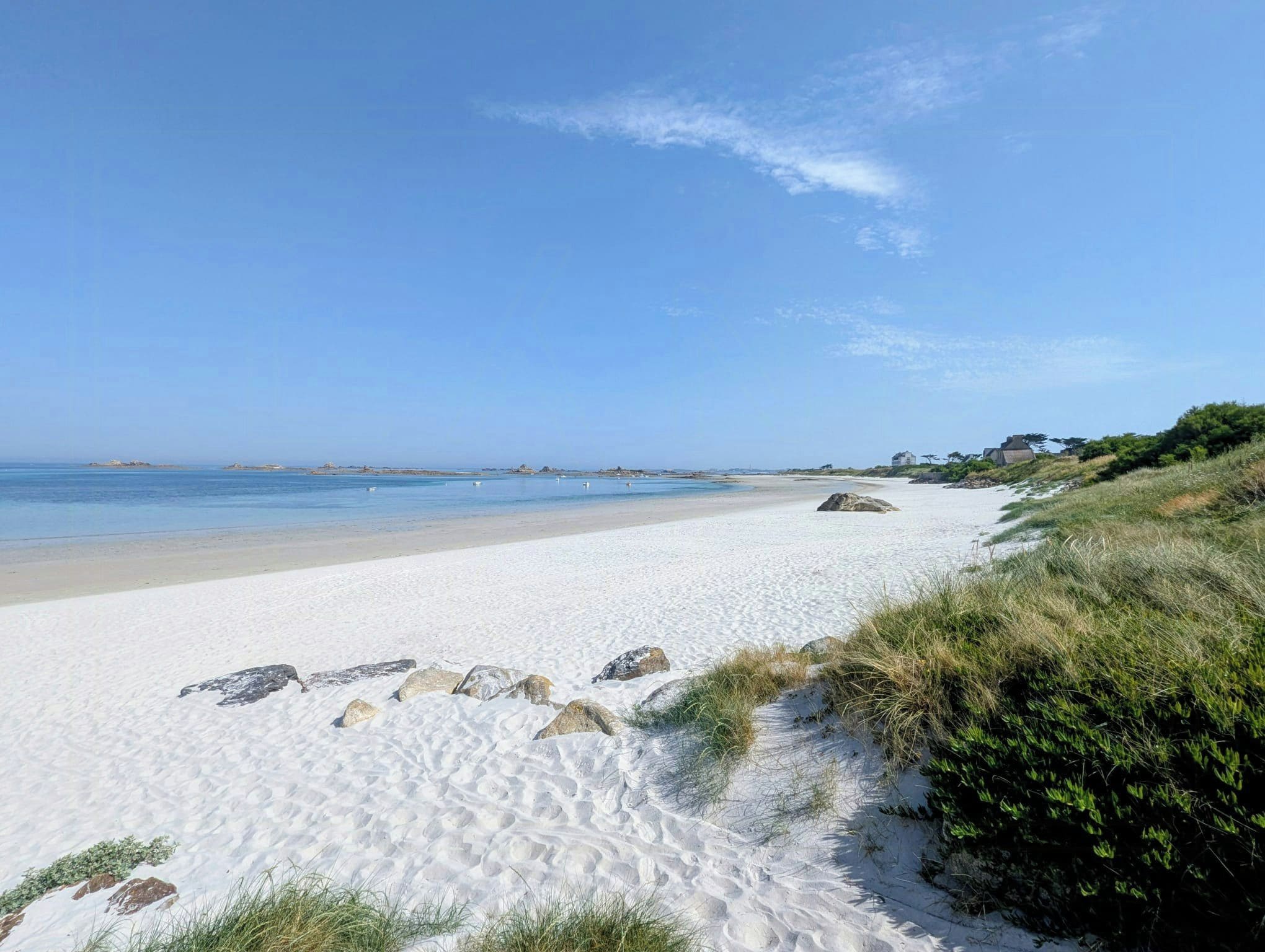 A beach with white sand, clear blue water, and a few scattered rocks.