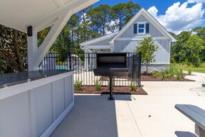 Ein überdachter Außenbereich mit Grill, Pool und einem Haus im Hintergrund.