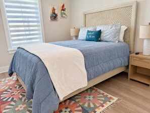 Ein Bett mit blauer und weißer Bettdecke, einer blauen Tagesdecke und einem Kissen mit Schriftzug. Ein Nachttisch mit Lampe und Fernbedienung ist ebenfalls vorhanden.