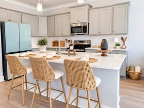 A modern kitchen with a central island, bar stools, stainless steel appliances, and light-colored cabinetry. - PCB Family Getaway, 3BR Townhome, Sleeps 6 - Community Pool (Panama City Beach)