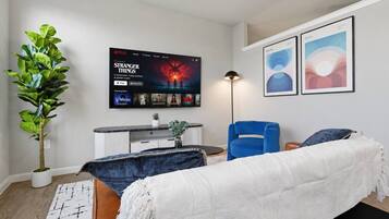 A modern bedroom with a bed, a blue chair, a TV displaying 'Stranger Things', and two framed artworks on the wall.
