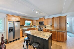 A modern kitchen with wooden cabinets, granite countertops, stainless steel appliances, and a bar area with stools. - New Rental! Relaxing 3-bedroom Lake Wawasee channel home in Johnson's Bay (Syracuse)