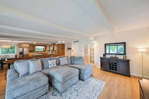 Ein Wohnzimmer mit einem Ecksofa, einem Fernseher und einer Küche im Hintergrund.