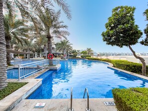 A swimming pool with a lifebuoy, surrounded by palm trees and a clear sky. - Stayshort - 2 Bed in Palm Jumeirah With Beach Access for 4 (Dubai)
