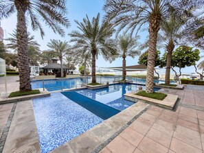 A swimming pool with tiled edges, surrounded by palm trees and a lounge area. - Stayshort - 2 Bed in Palm Jumeirah With Beach Access for 4 (Dubai)